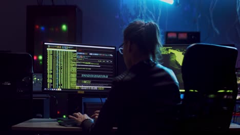 parte trasera de la hermosa desarrolladora o hacker en las gafas programando virus o antivirus en la computadora en la sala de software oscura con alta tecnología