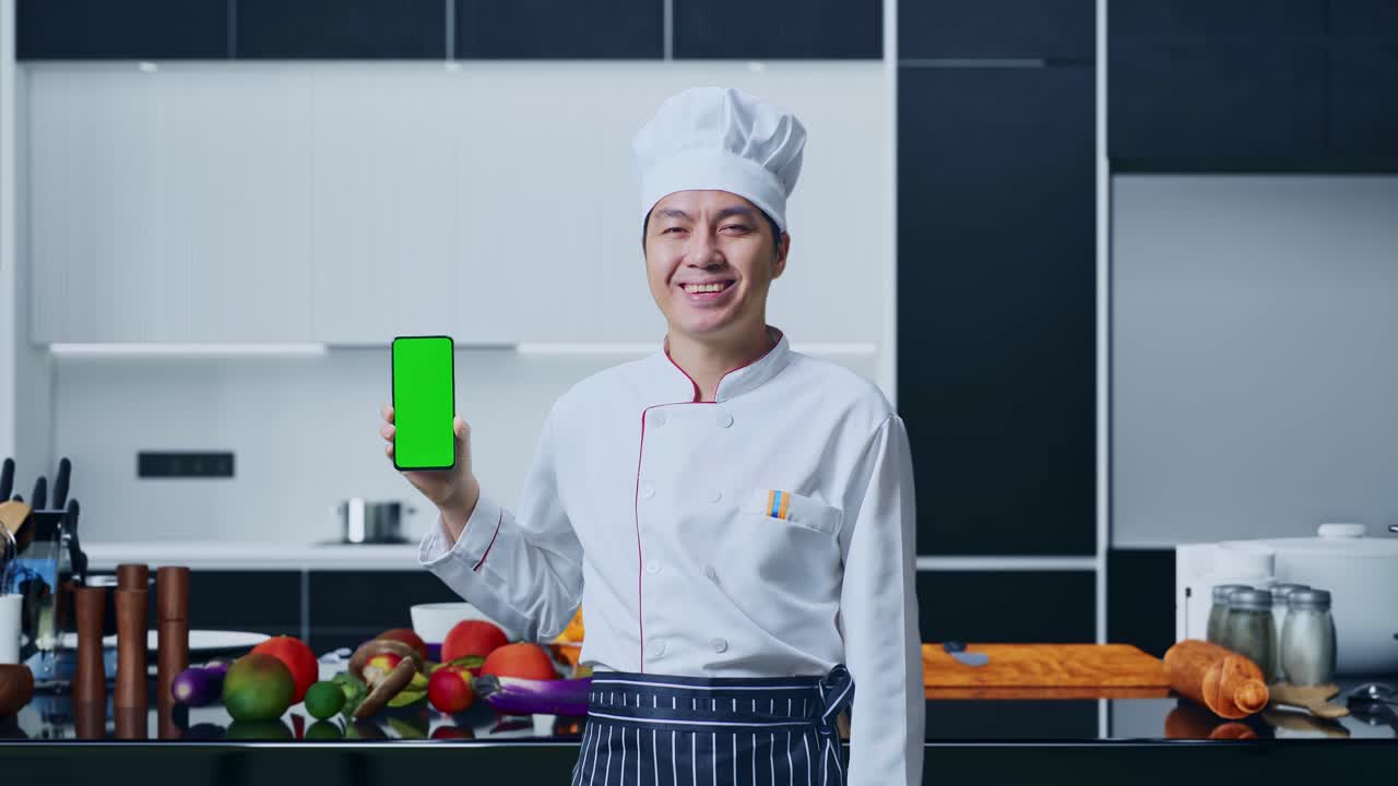 chef con teléfono inteligente de pantalla verde en la cocina