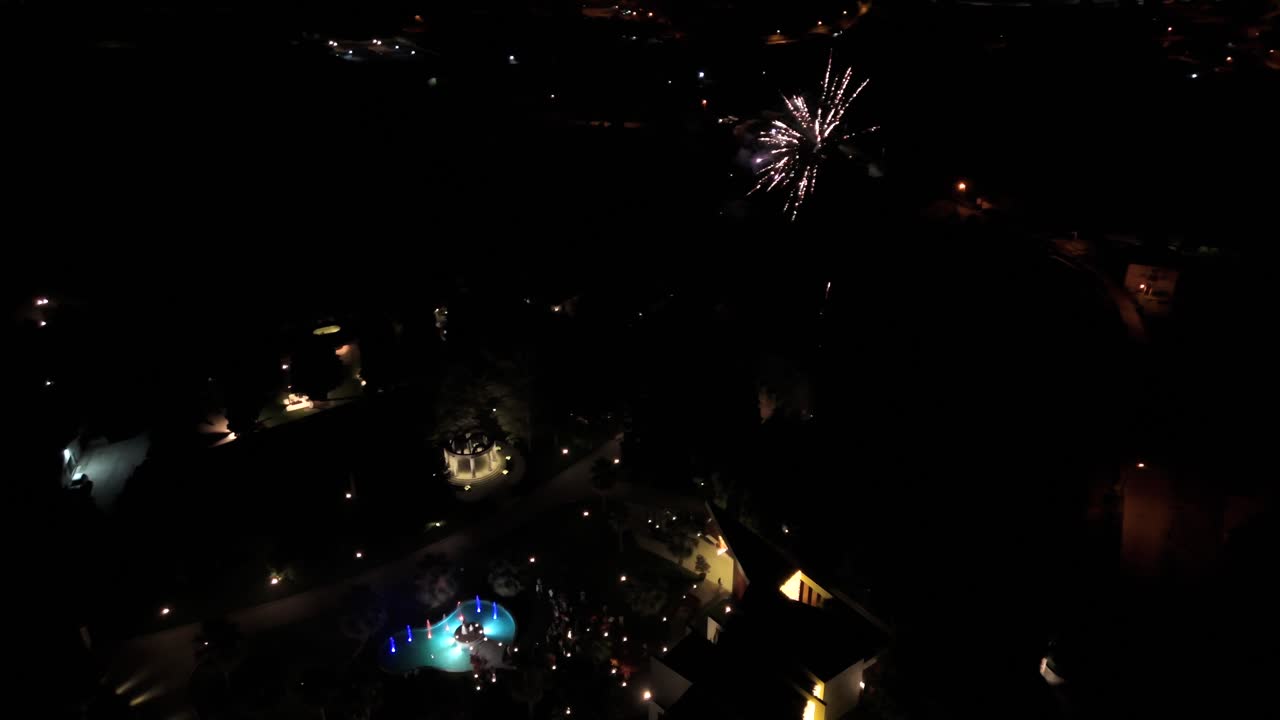 la novia y el novio cortan pastel por la noche junto a una laguna, fuegos artificiales iluminando el cielo