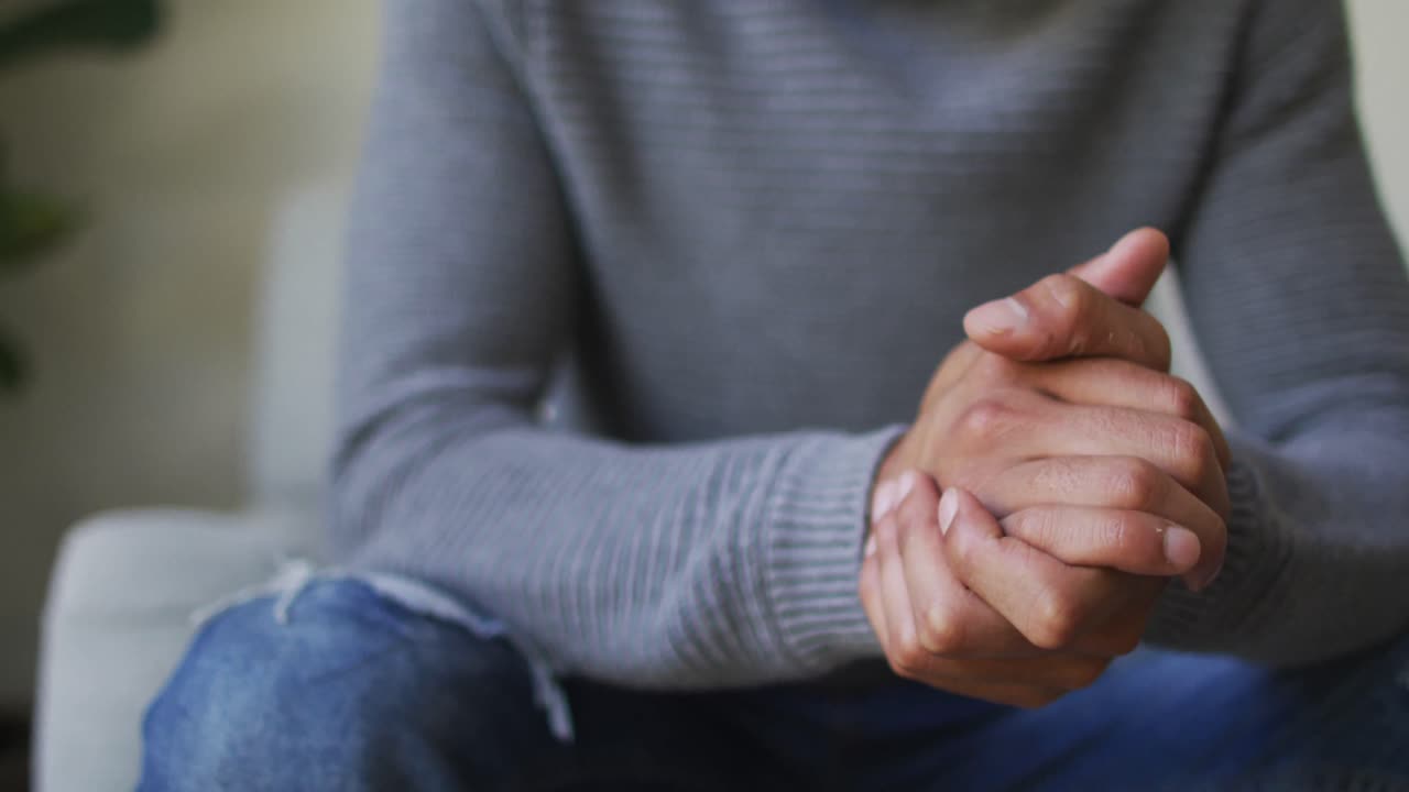 hombre biracial pensativo con dreadlocks en el peluche sentado en la sala de estar mirando hacia otro lado