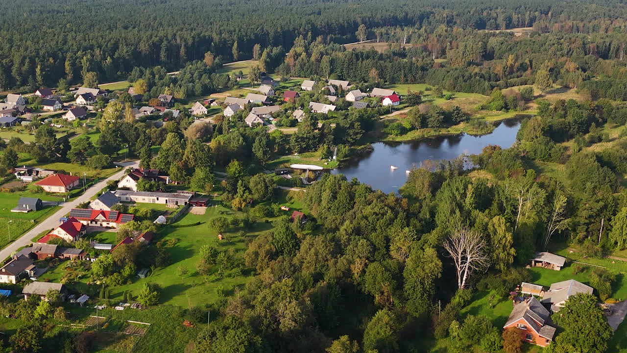 Aerial video of small rural village in Pavilosta Latvia with pond and surrounding trees.
