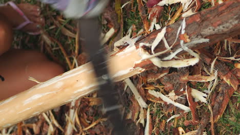 woman shaving bark off large stick with machete, vertical close up, slow motion