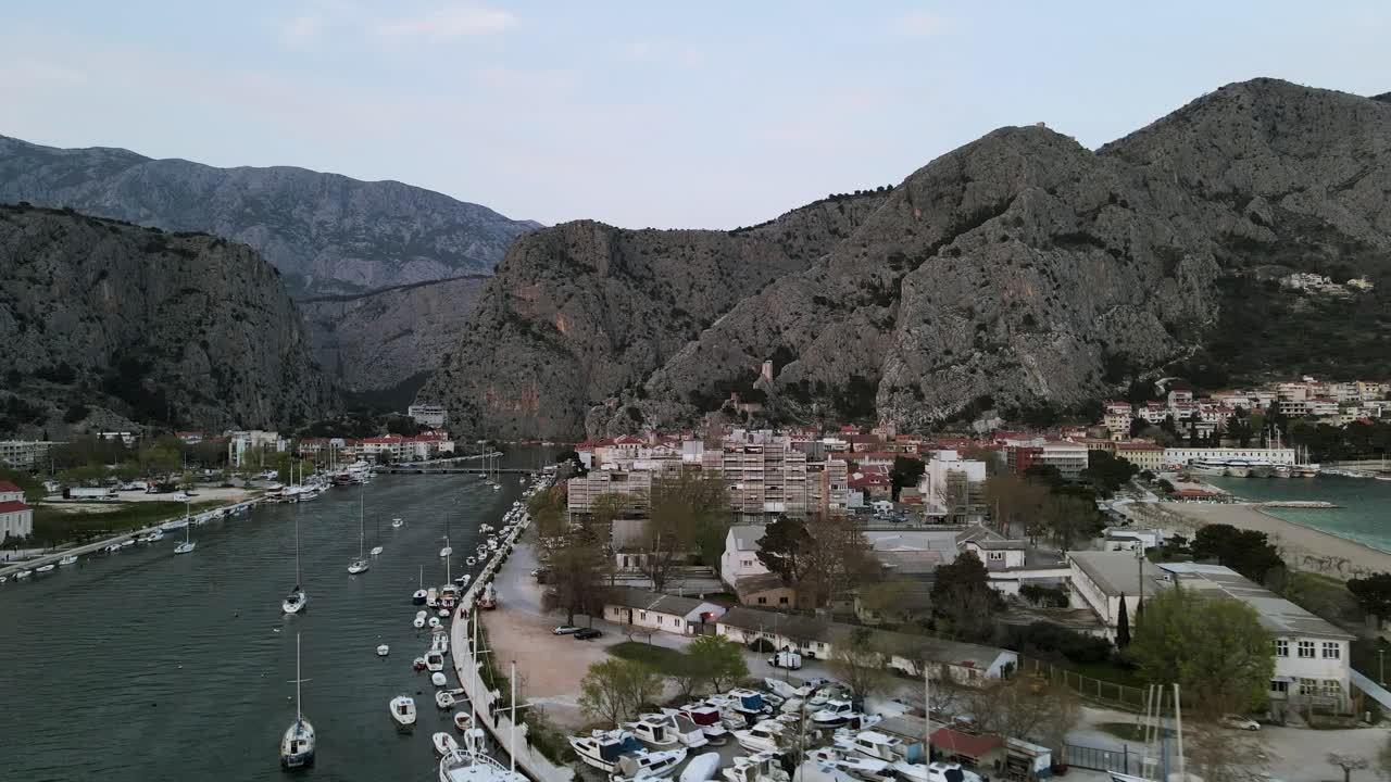 Boats docked along Omis town promenade, Cetina river. Town against beautiful mountain gorges.
