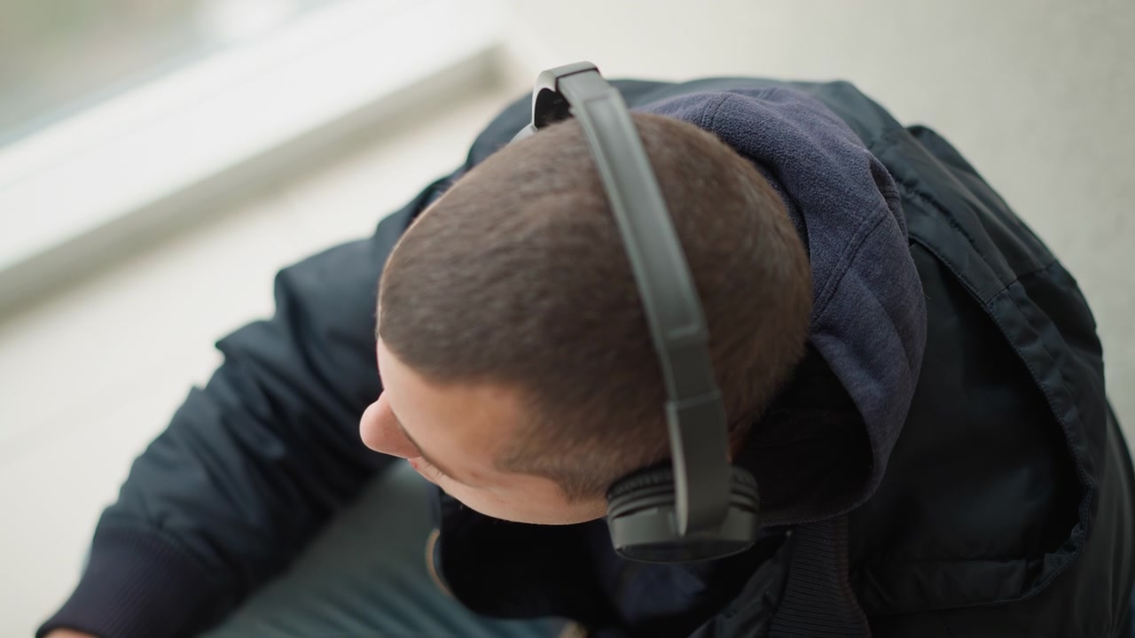 Nærbillede af mand med hovedtelefoner, der hviler hovedet på en usynlig overflade med minimal bevægelse. Personen er klædt i mørkt tøj, og baggrunden forbliver ude af fokus