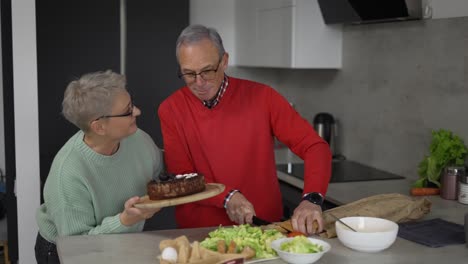 Elderly-woman-wife-making-surprise-for-husband-giving-birthday-cake-to-him-on-the-kitchen
