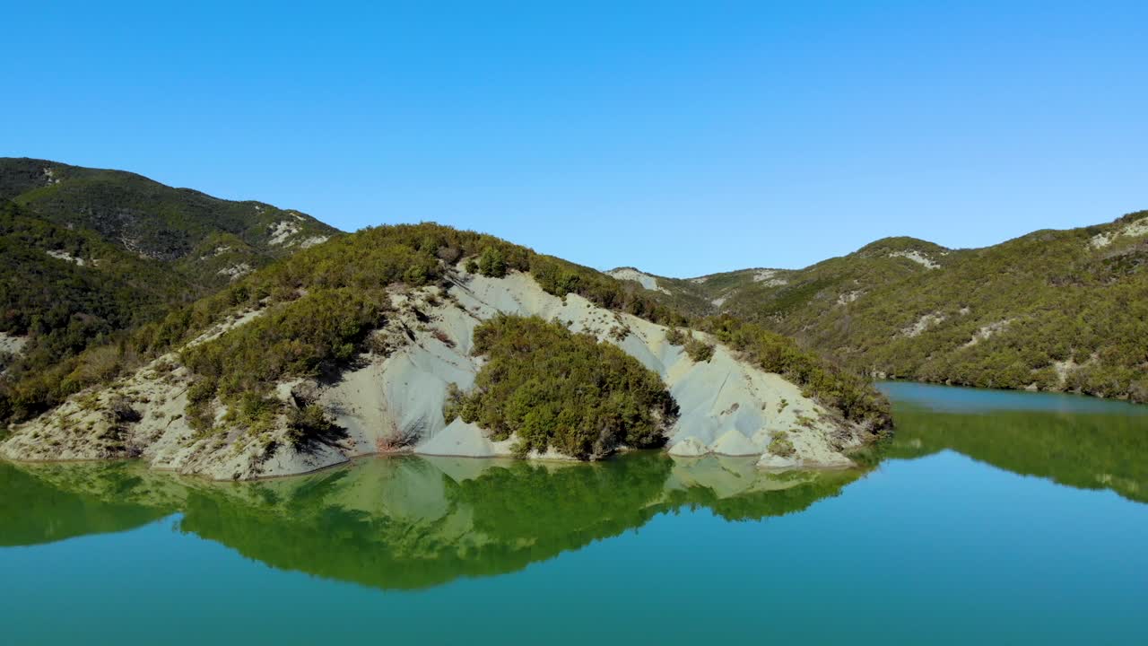 Paradise alpine lake on high mountains with green lush vegetation slopes and clear blue sky reflecting over calm water