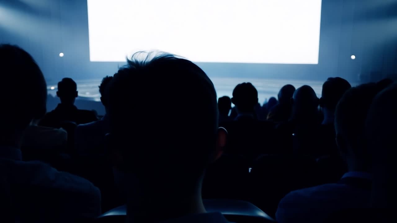 el público mira una pantalla blanca en blanco en un auditorio oscuro, creando una atmósfera dramática para presentaciones y eventos