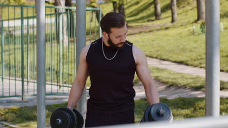 athletic man doing arms weight lifting dumbbells exercises, pumping up arm bicep muscles outdoors