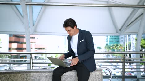 confident businessman using laptop working outdoors in the financial district in the city. using phone talking to client solving problems