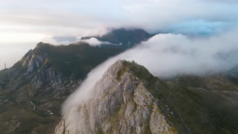 Nubes-Moviéndose-Sobre-Picos-Montañosos-Y-Entre-Montañas-Con-Puesta-De-Sol-Al-Fondo.