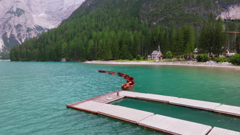 aerial shot of lago di braies under a cloudy spring sky, with wooden boats creating gentle movement on the water. the cappella lago di braies is in view