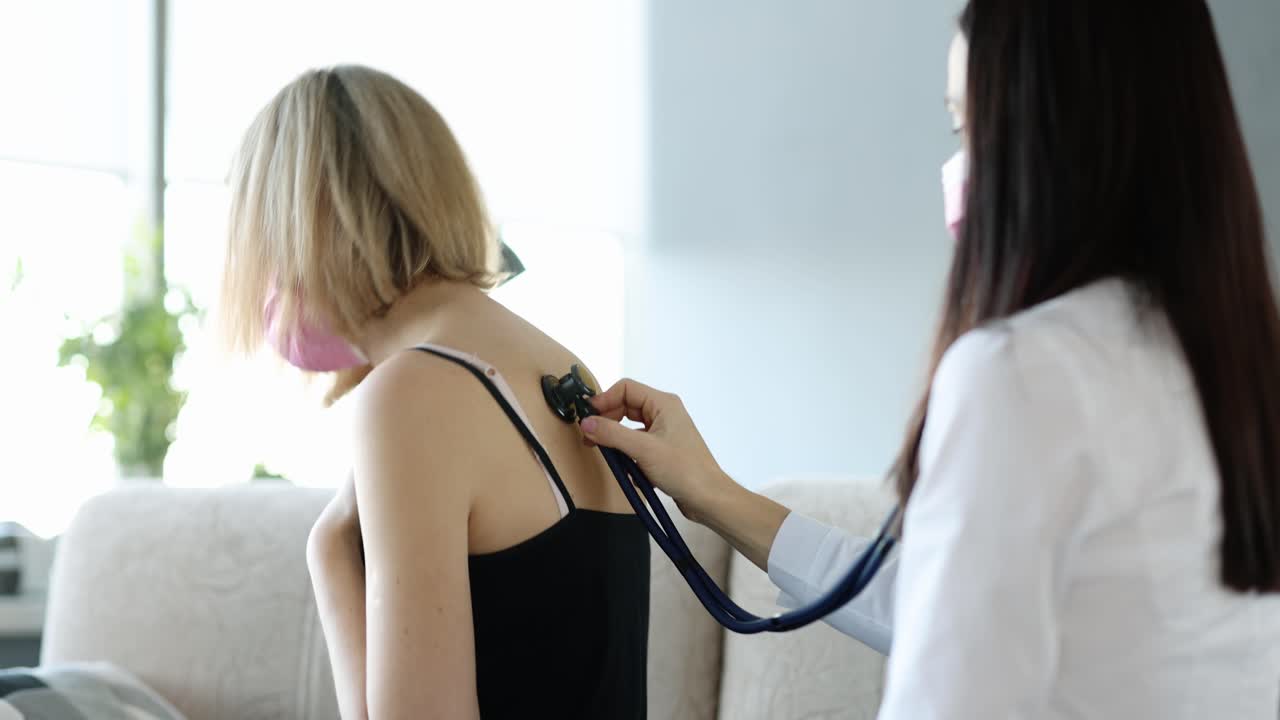 Doctor examines and listens to lungs of woman coughing strongly at home