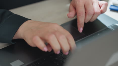 Close up of woman hands typing on laptop keyboard with pink painted nails, black sleeve visible, partial blur of blue folder in corner, soft lighting adds subtle background
