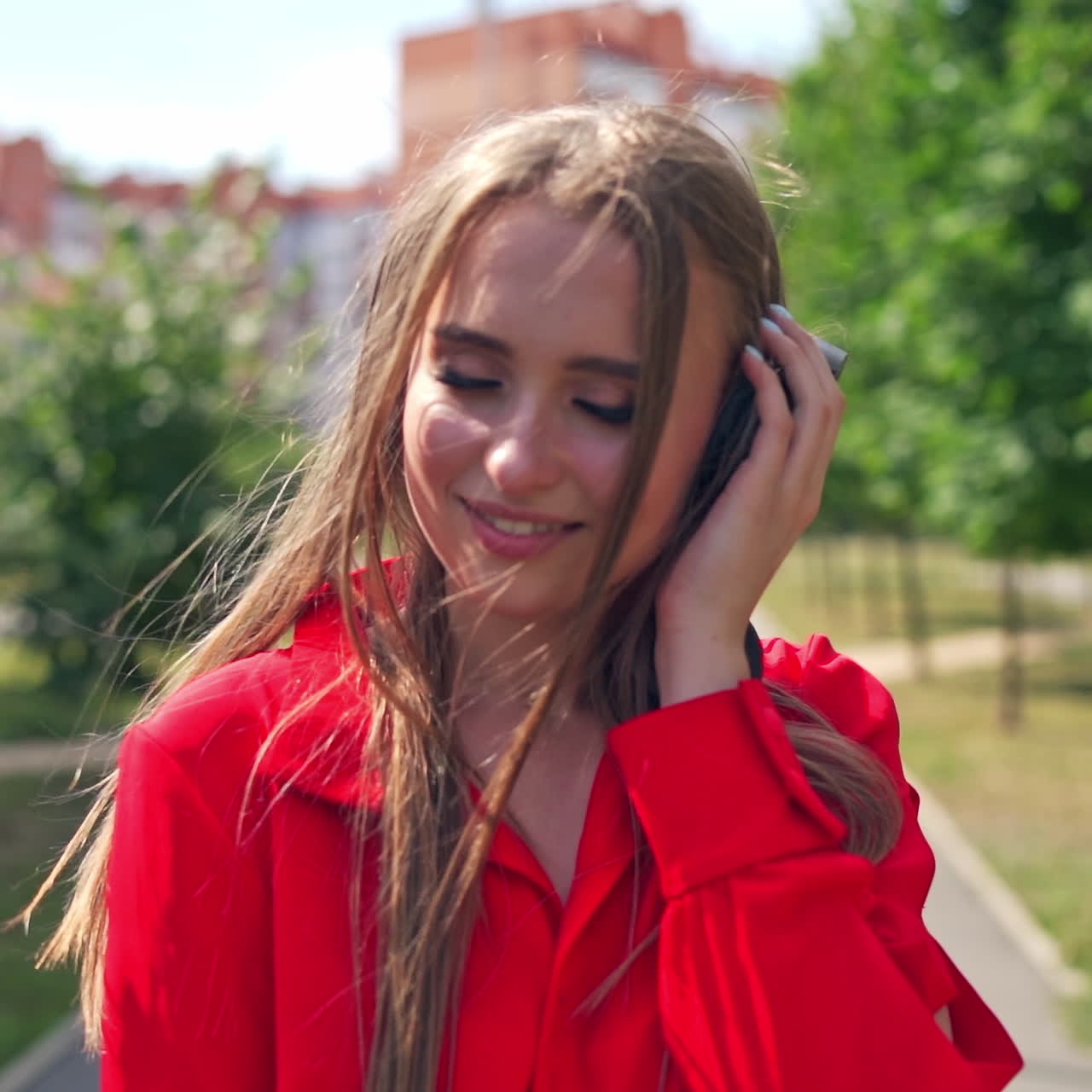 Beautiful girl with headphones walking in the city. Young woman with long hair listening to music through the headphones outdoors. Slow motion.