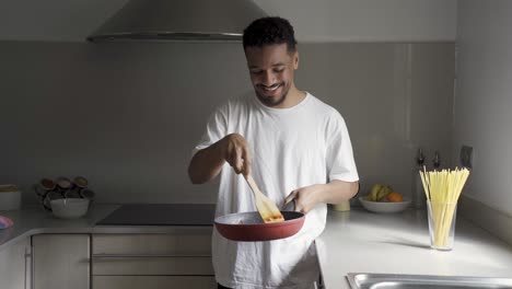 content ethnic man frying tomatoes on pan in kitchen