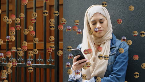 emojis de cara que se mueven contra la mujer en hijab usando un teléfono inteligente