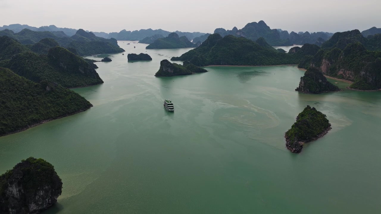 Vịnh Hạ Long Việt Nam, cảnh quay trên không nghiêng xuống một du thuyền đơn độc di chuyển trên mặt nước tĩnh lặng giữa các đảo đá vôi nhiệt đới.