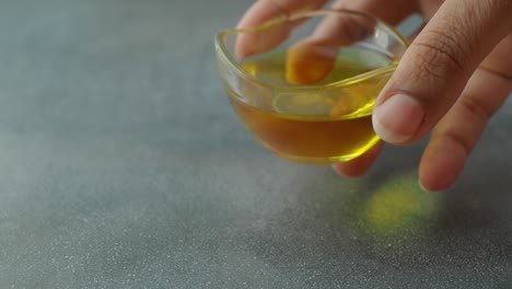 close-up of a hand holding a small glass bowl of cooking oil