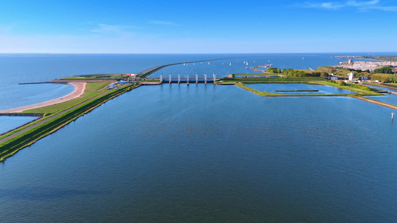 Smooth surface of lake Markermeer in Lelystad, the Netherlands. View on dams with sluices and sailboats at backdrop.