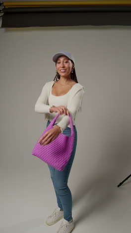 vertical video of female social media influencer producing user generated content in studio catching and modelling purple bag 1