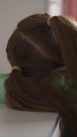 tired girl with long ponytails lies on desk with school supplies in children room little student