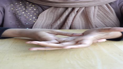 closeup of a woman's hands with a hijab, sitting at a table.