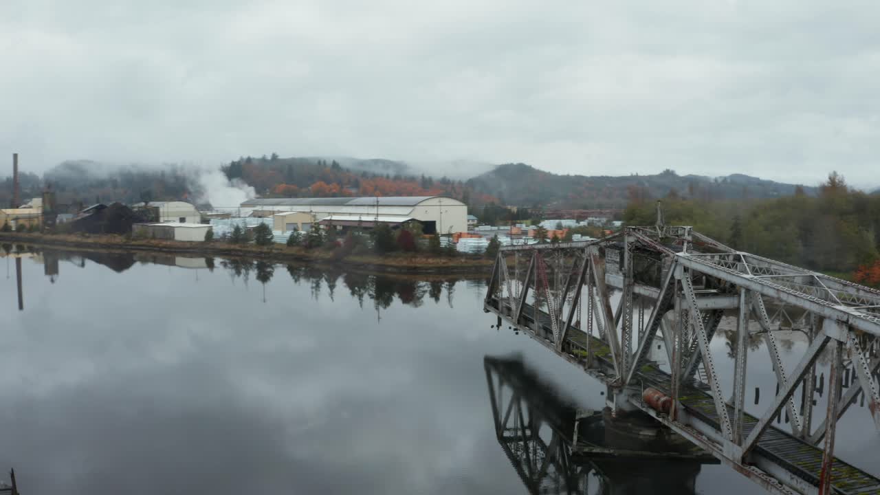 órbita aérea del antiguo puente giratorio en medio de un lago brumoso cerca de una pequeña fábrica