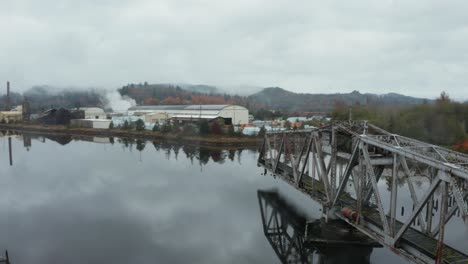 aerial orbit of old swing bridge in the middle of foggy lake near small factory