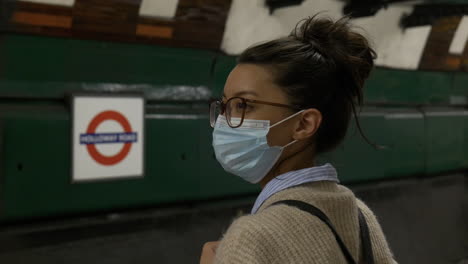 woman wearing a face mask is waiting for a tube train in a london underground station