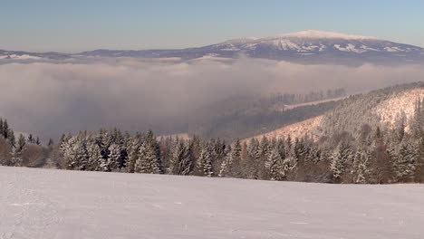 Slow-tilt-up-over-magical-winter-landscape-with-snowy-hill,-trees-and-mountain