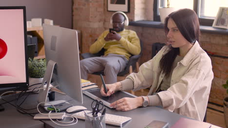 femme graphiste concentrée utilisant une tablette de dessin numérique et regardant un moniteur dans un studio d'animation