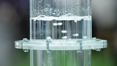 hydrogen gas bubbeling through a membrane in a plastic cylinder filled with water, small bubbles forming in liquid, slow motion