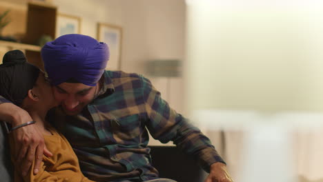 Loving-Sikh-Father-And-Son-Wearing-Turbans-Sitting-On-Sofa-At-Home-Talking-Together