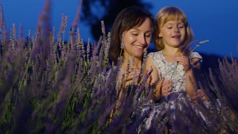 mother enjoying time with child daughter girl, touching sniffing aromatic flowers in lavender field