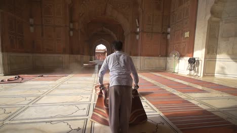 man shaking dust off of prayer mats