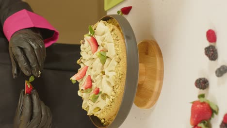 vertical shot of hands starting to decorate red berry pie with strawberries