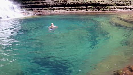 joven nadando en agua azul clara de cascada desde el ángulo superior