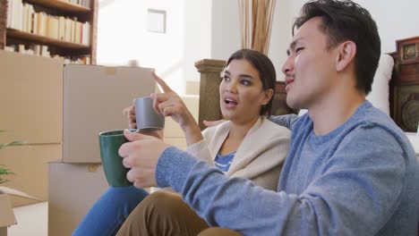 video of happy diverse couple drinking coffee in new house after moving in