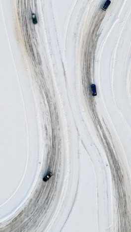 portrait drone shot above cars racing on a snowy ice road, sunny, winter day