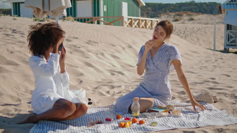 lgbt couple taking photos on sandy seashore. two happy girls having picnic fun