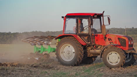 side view of a red tractor cultivating the soil on the field. farmer in tractor prepares land for sowing in farmlands outdoors.