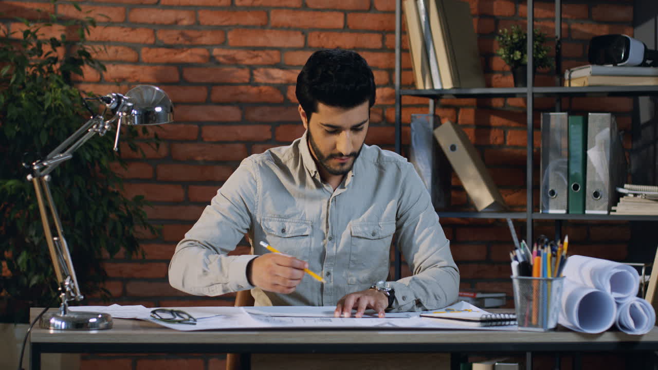 arquitecto árabe dibujando un plan de construcción en el escritorio de su oficina, luego levanta la cabeza y sonríe a la cámara
