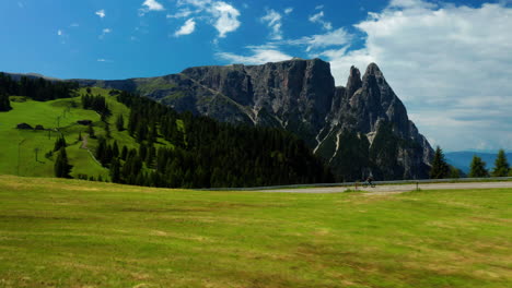 Flying-over-mountain-plateau-as-Man-bikes-Dolomites-Road,-Italy