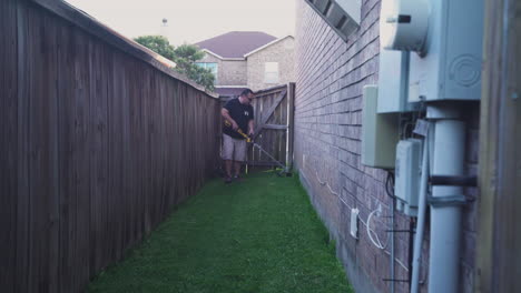 a latino trimming his lawn of the side of his house in the late afternoon