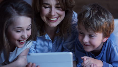 close-up view of caucasian mother and his little son and daughter lying on the bed and watching something on the tablet