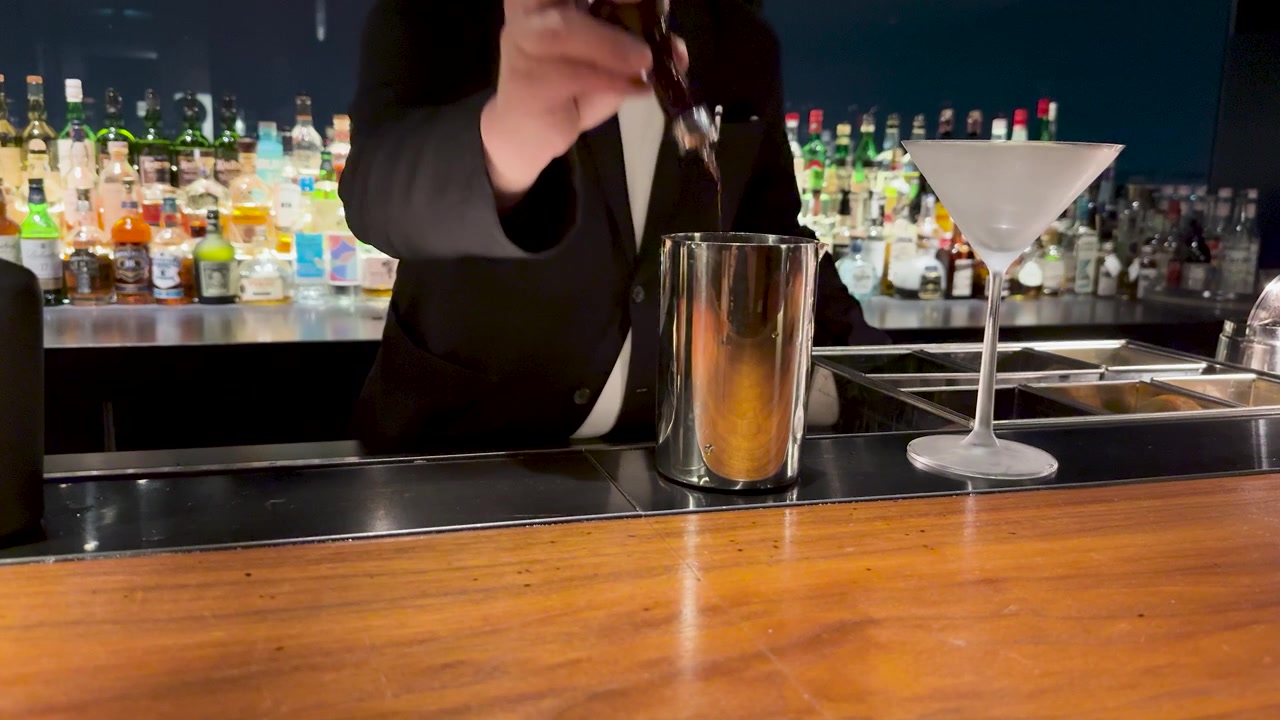 Un Barista Professionista in Abito Nero Aggiunge Bitter a uno Shaker in un Bar