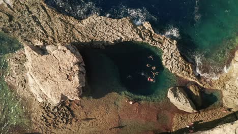 Aerial-view-of-people-swimming-in-a-pristine-blue-sea-in-the-famous-Blue-Hole-in-Dwerja-on-the-island-of-Gozo,-Malta