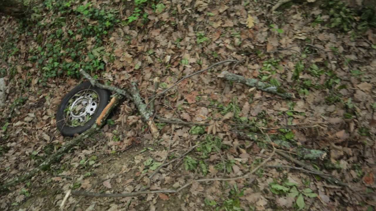 vecchia ruota di automobile abbandonata sul terreno della foresta con foglie e rami in modo non ecologico, ripresa ad alto angolo medio ravvicinato