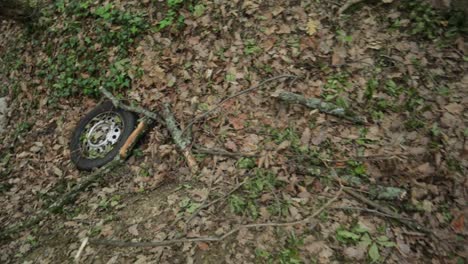 rueda de coche vieja abandonada en el suelo del bosque con hojas y ramas de una manera no ecológica, tiro de ángulo alto de primer plano medio