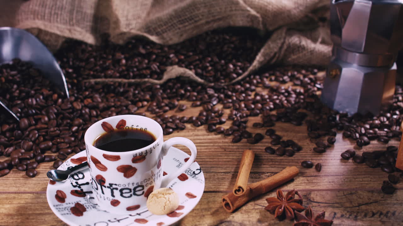 Pack shot - Camera moving down towards a freshly poured espresso cup with cinnamon, star anise and freshly roasted coffee beans on a wooden table